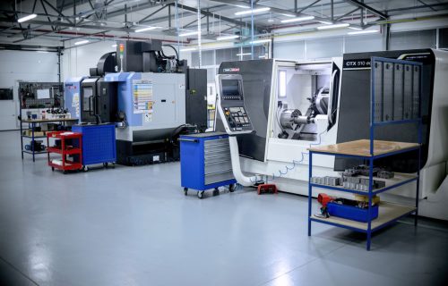 Production hall equipped with large CNC machine tools, blue tool trolleys and a clean grey floor.