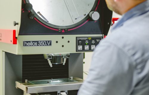 Operator at an optical measuring projector with a round screen displaying the magnified contour of the inspected component.