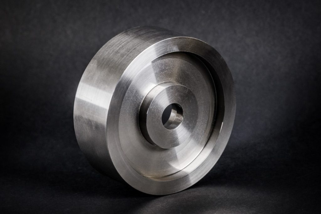 A disc-shaped turned metal part with a raised hub and central hole, shown against a dark background.