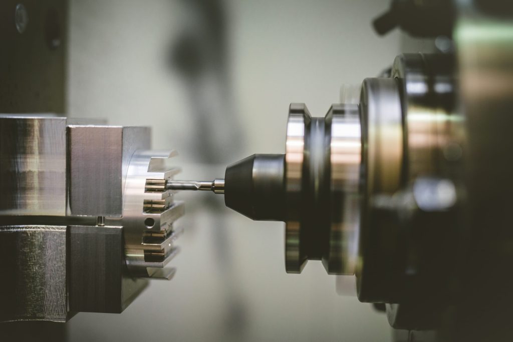 A precision drill bit machining a metal component held in a CNC machine against a light background.