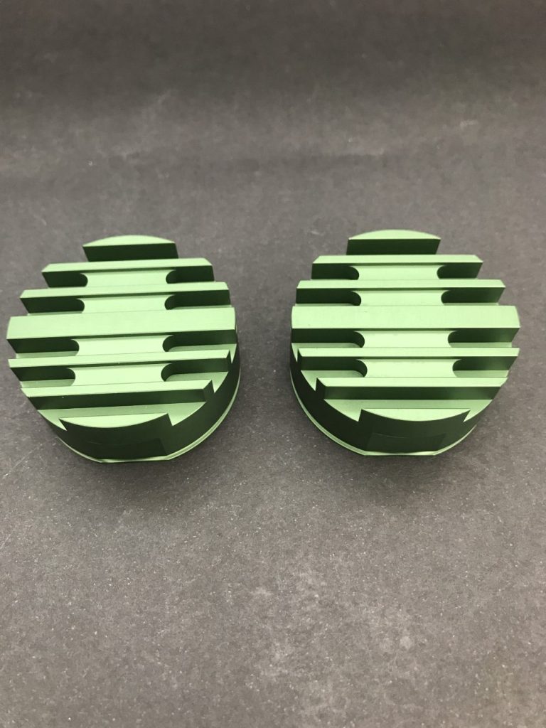 Two green round metal components with numerous milled grooves, lying side by side against a dark background.
