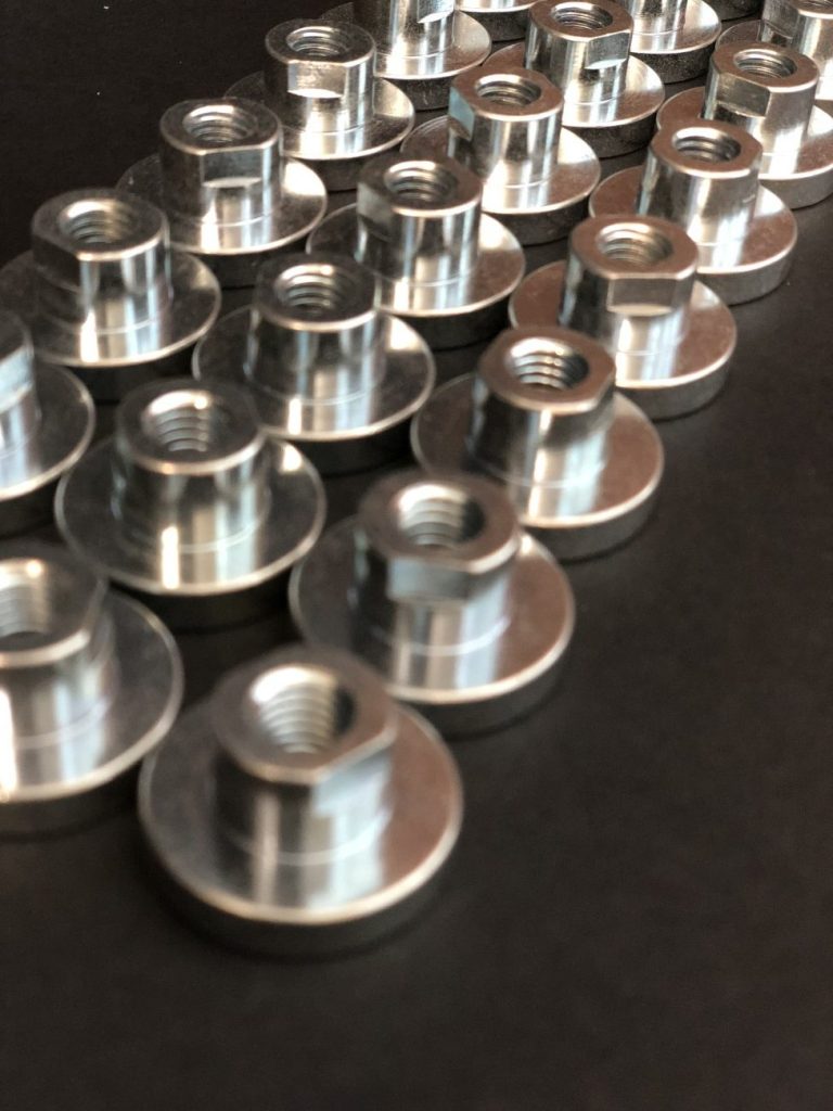 Metal flange nuts with internal threads, polished to a high gloss and arranged against a dark background.