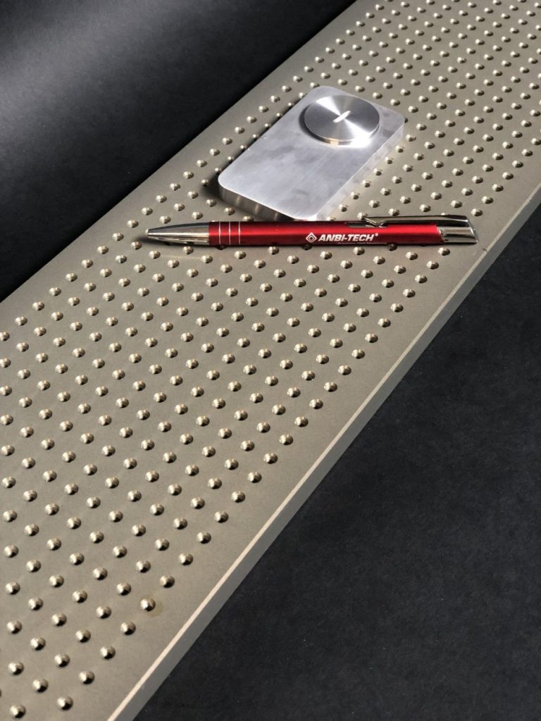 A metal plate with densely arranged holes, with a milled component and red pen resting on it.