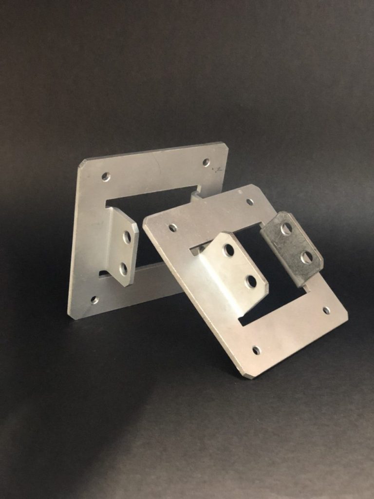 Two silver metal mounting components with cut openings and bent wings, standing against a black background.