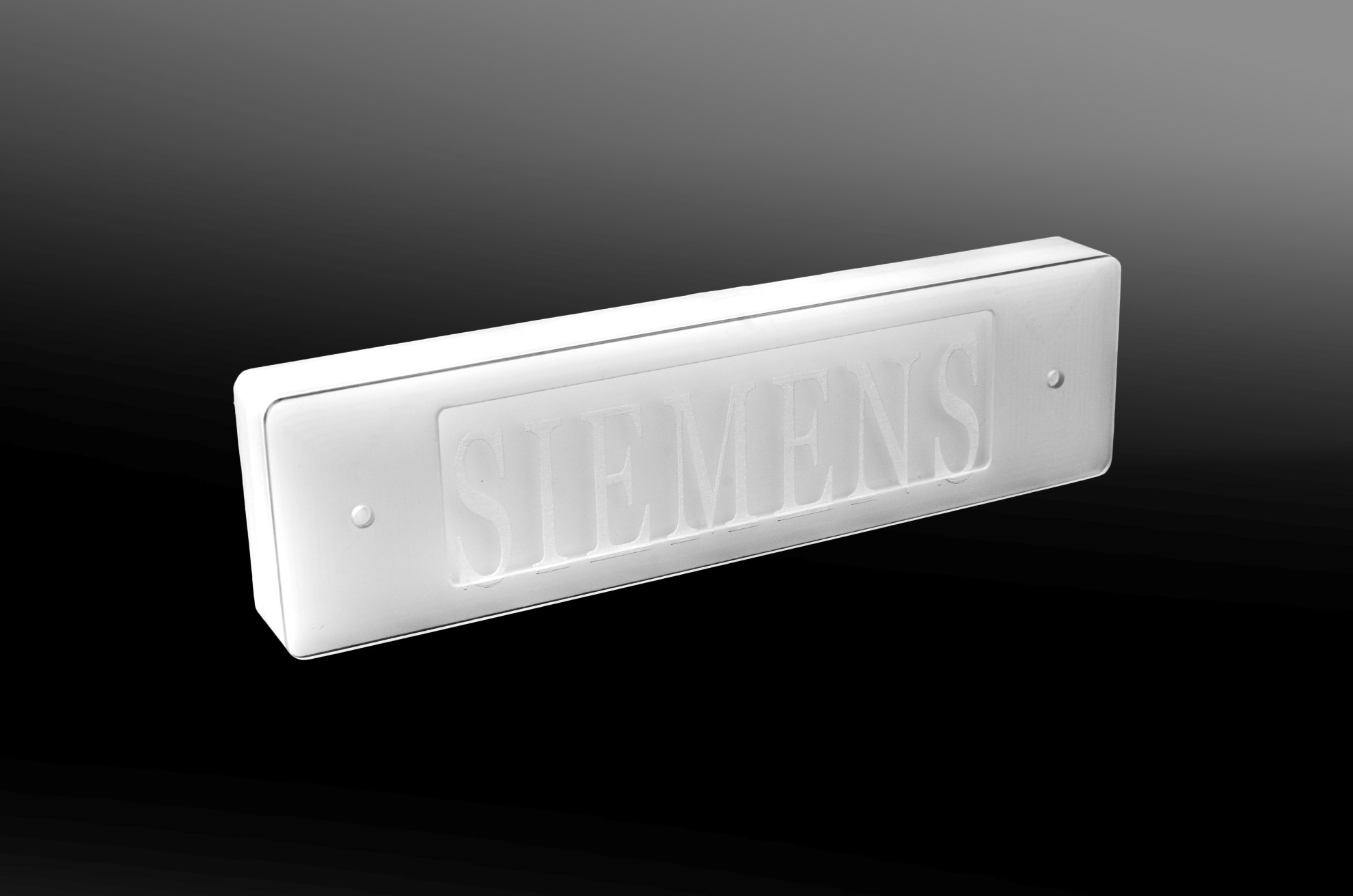 A white rectangular component with embossed SIEMENS lettering and two small holes, shown against a dark gradient background.
