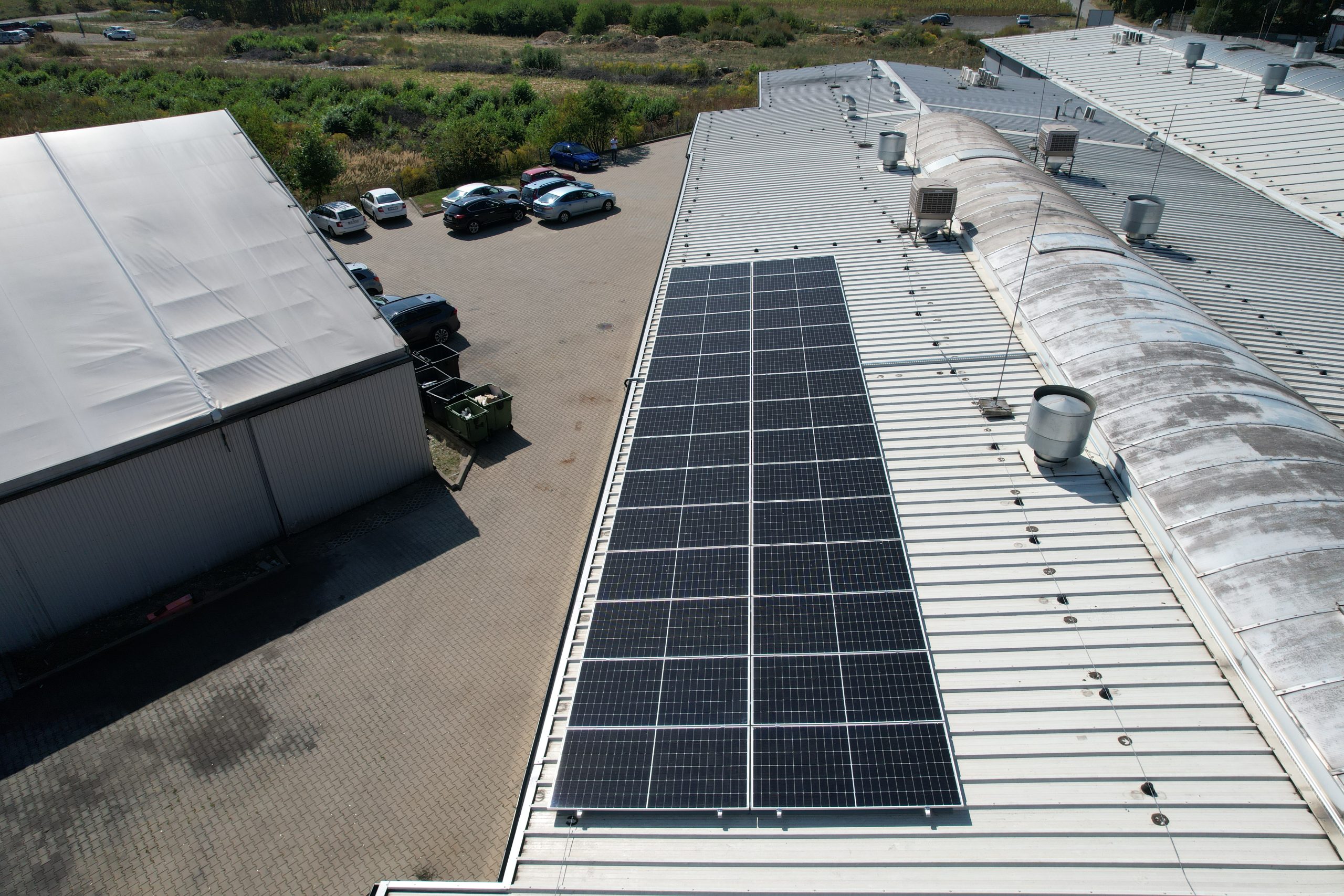 Photovoltaic panels mounted on the metal roof of the production hall, with a car park visible alongside.