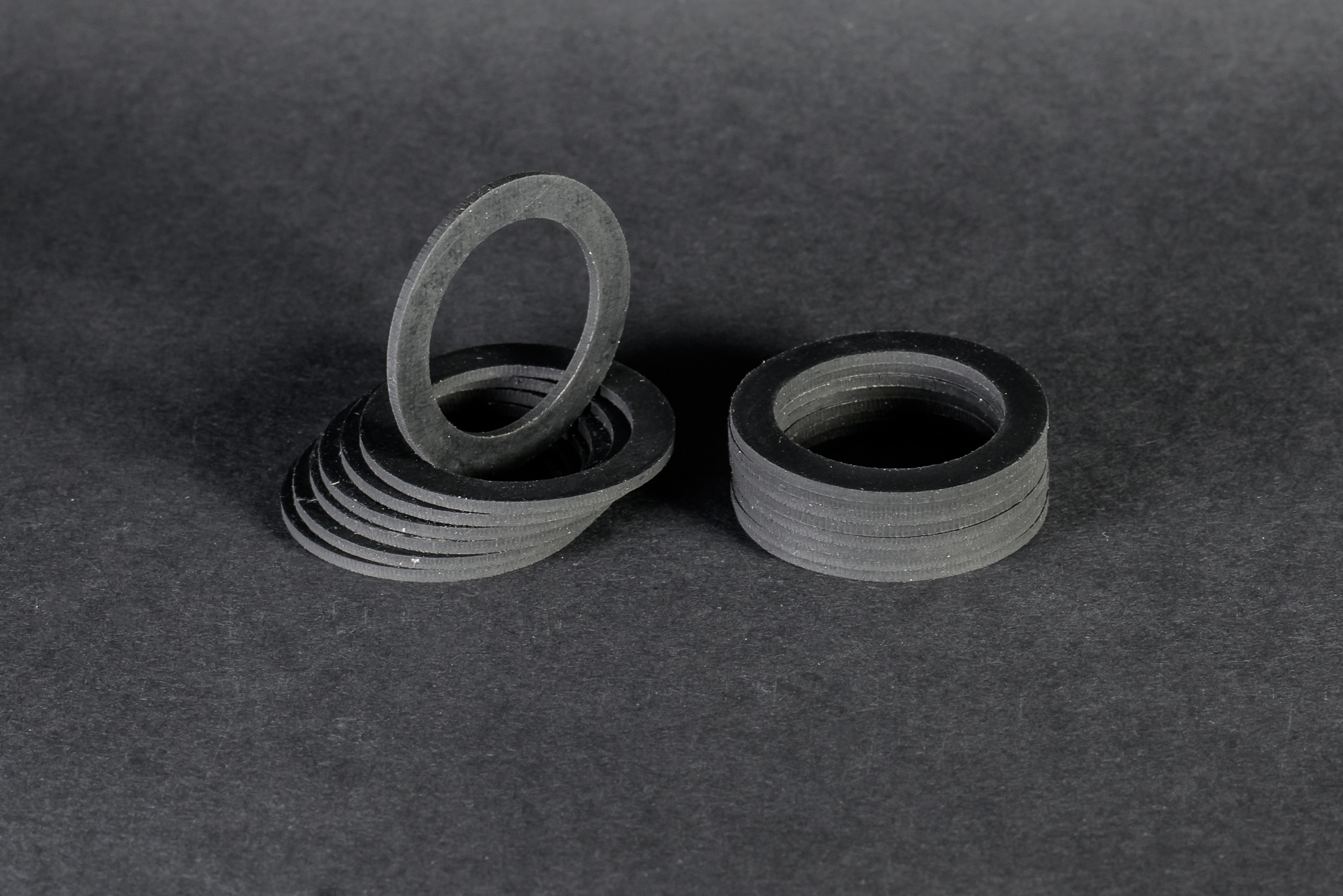 Two stacks of black, matt, flat rings stand against a dark grey background, with one ring resting upright.