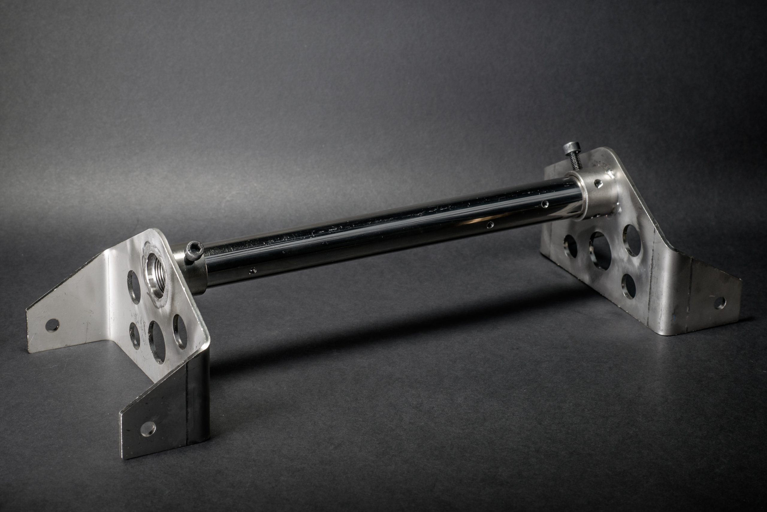 Metal structural component with a polished shaft and two bent brackets with holes, set against a dark background.