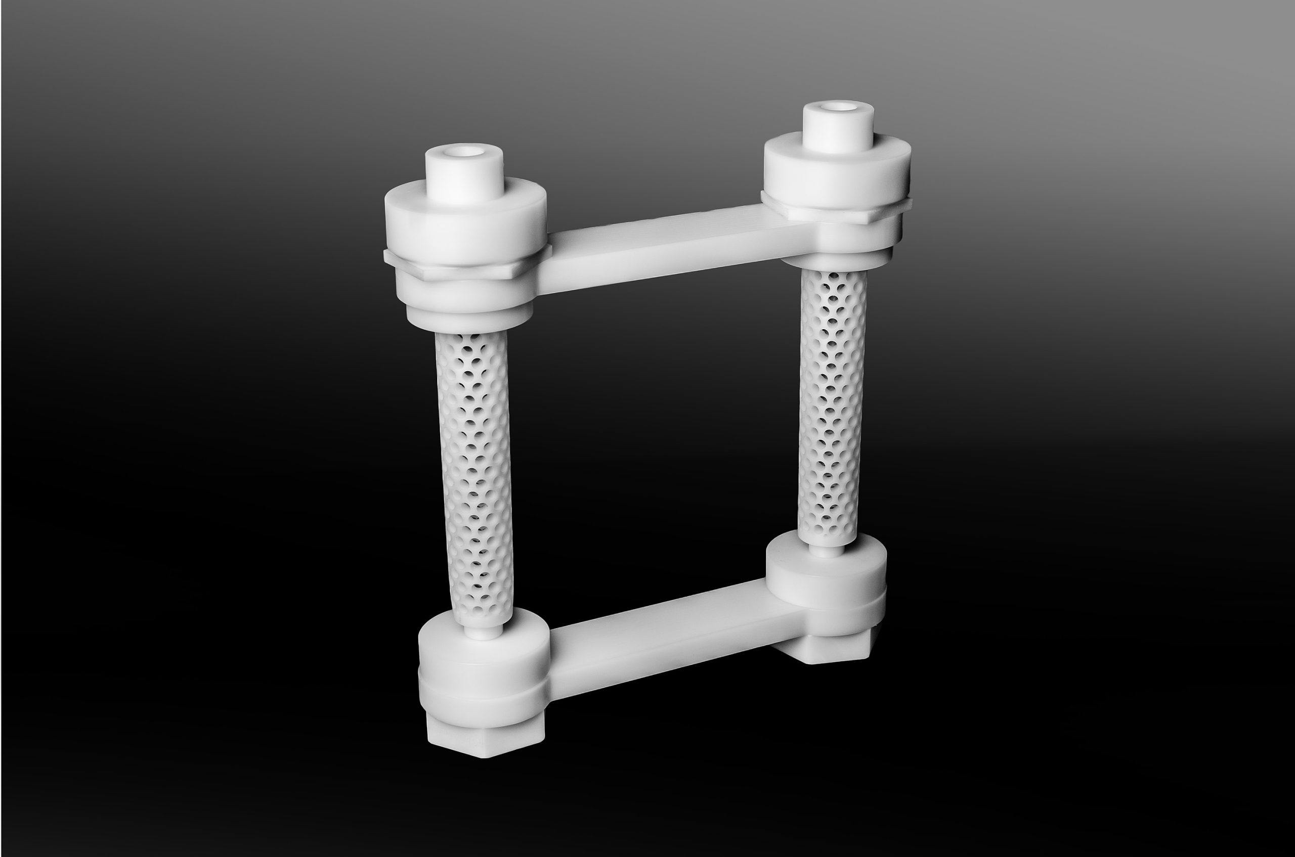 White plastic component consisting of two perforated rollers and connectors on a dark background.