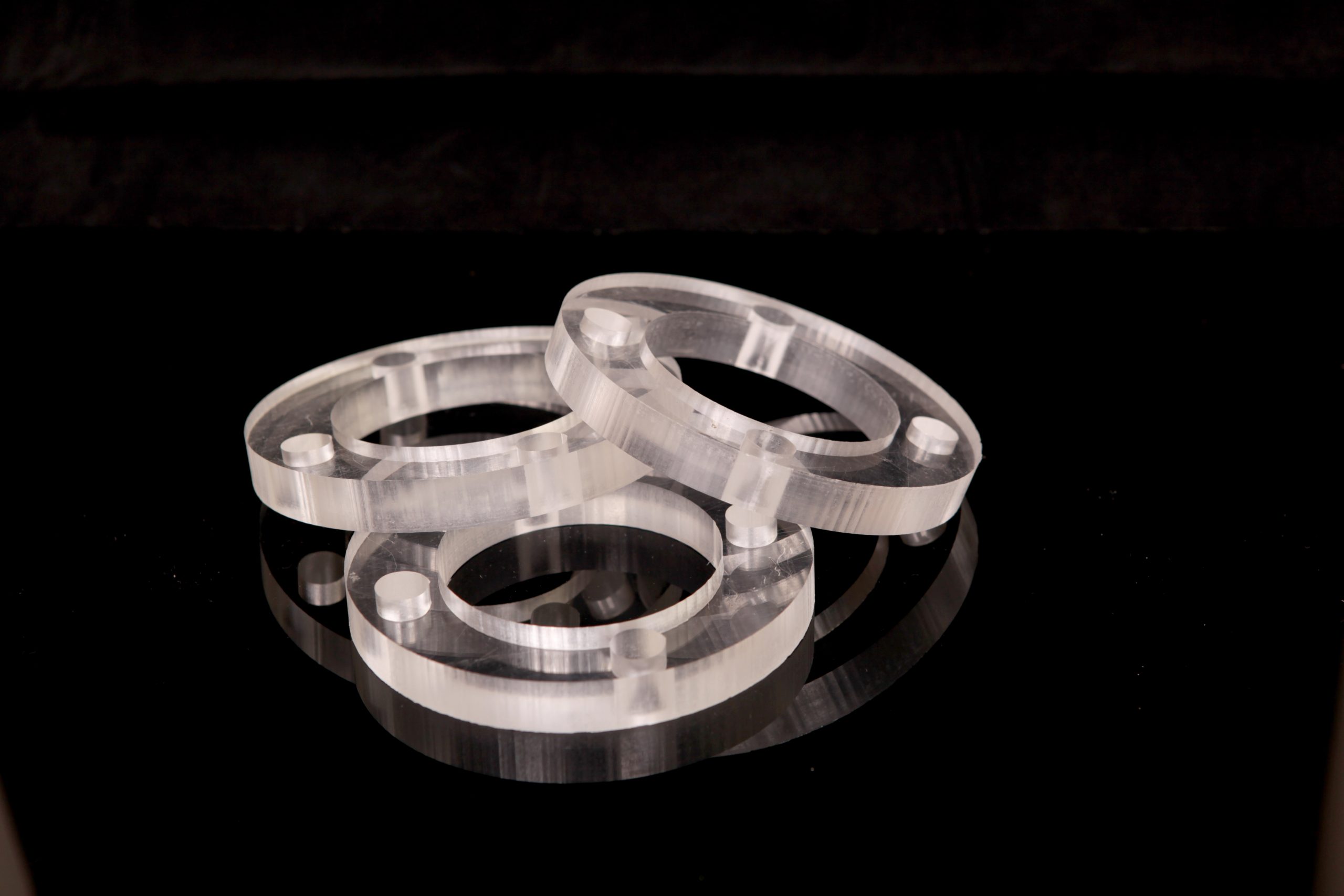 Three transparent rings with small pins lying on a black surface, reflected in the mirror-like sheet.