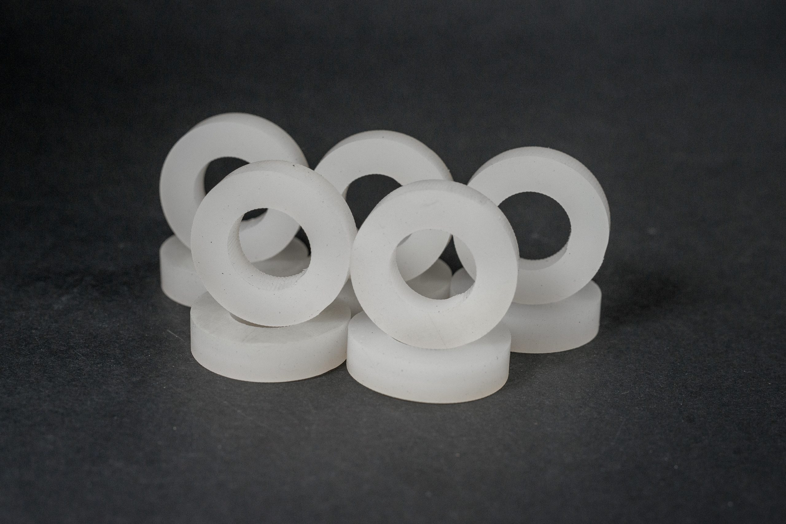 A group of turned white plastic rings with central holes standing on a dark surface.