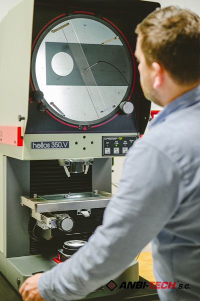 An operator inspecting the quality of a machined component on an optical projector with a round screen in the measuring room.