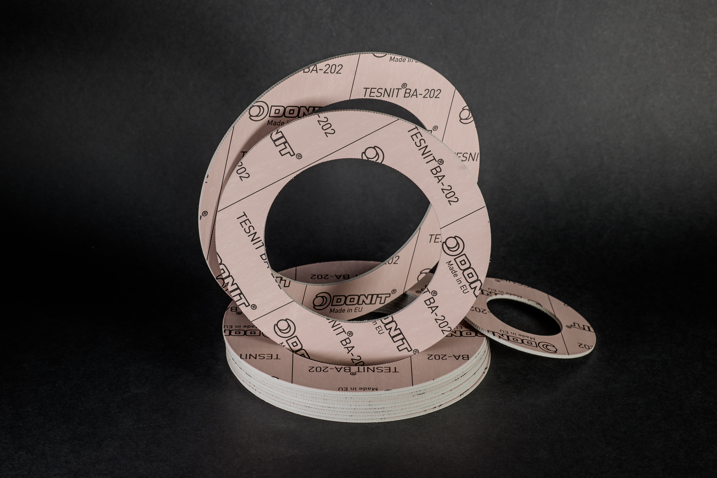 Flat sealing rings cut from a composite sheet, stacked and leaning against a black background.