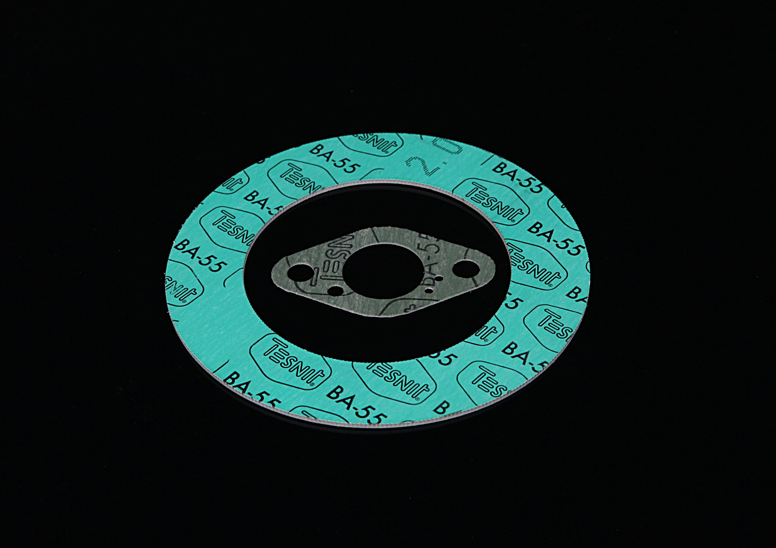 Green round gasket and a smaller sealing flange with holes, placed side by side on a black background.