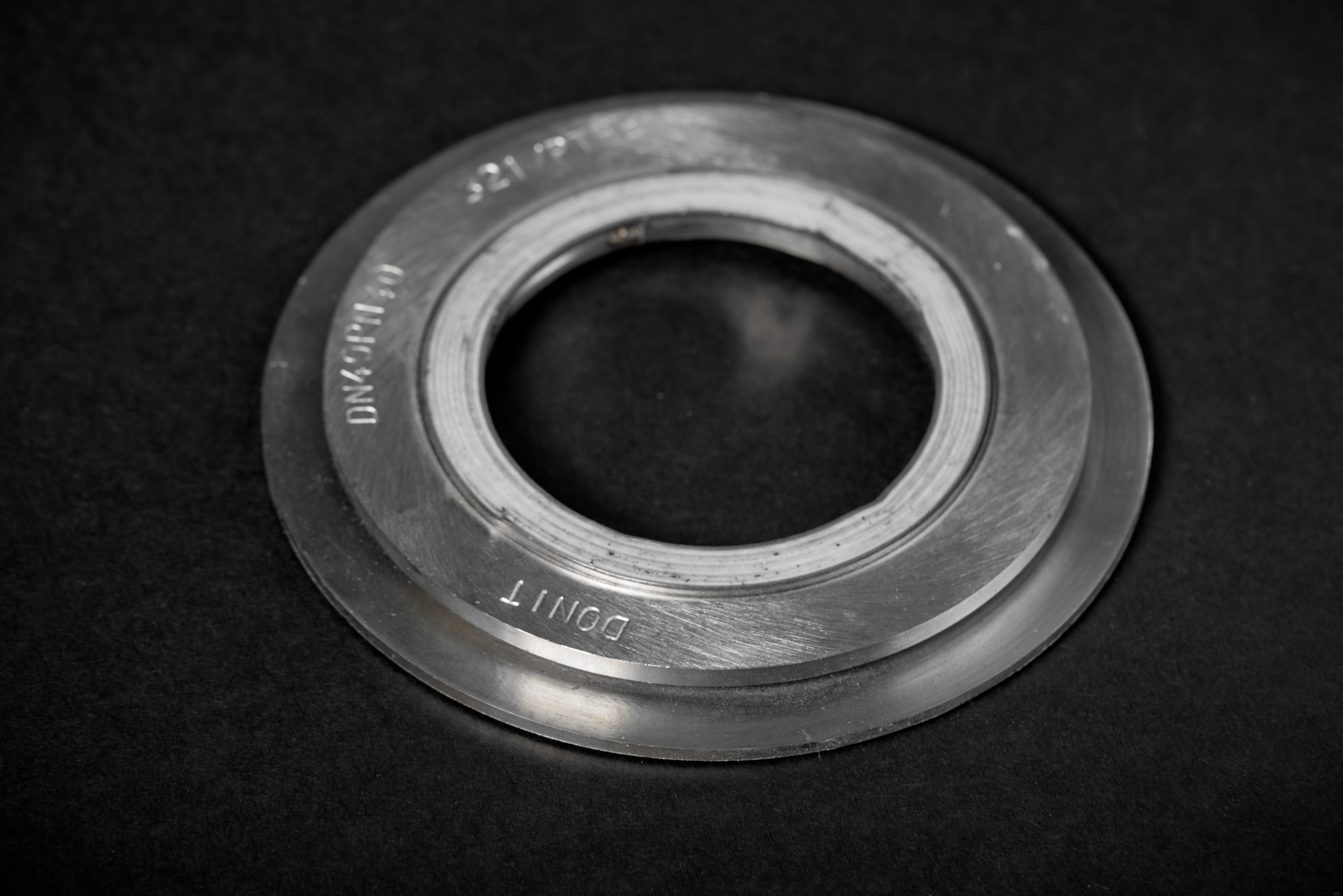 A metal spiral wound gasket with markings engraved on its surface, set against a matt black background.