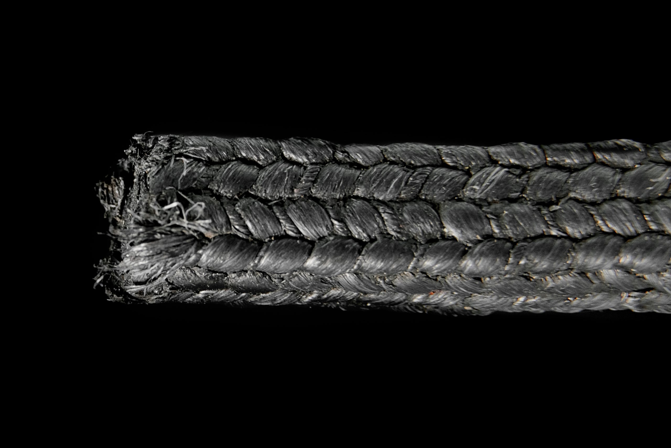 Dark grey, thickly braided cord with a frayed edge on the left side, shown against a uniform black background.