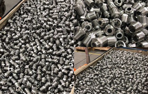Silver threaded metal fittings with a hexagonal section, poured in large quantities into a wooden crate.
