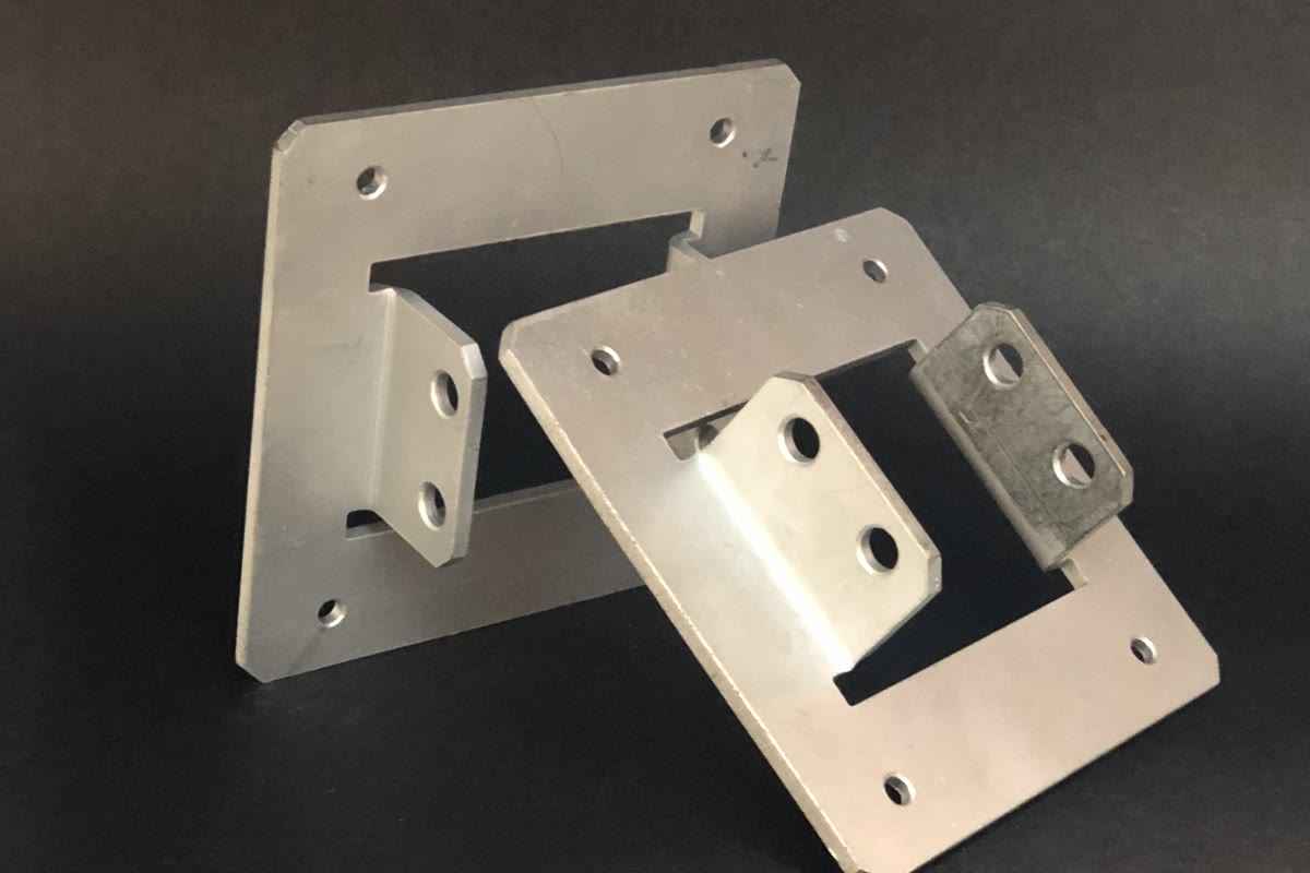 Two silver metal components with rectangular cut-outs, holes and protruding sections on a black background.