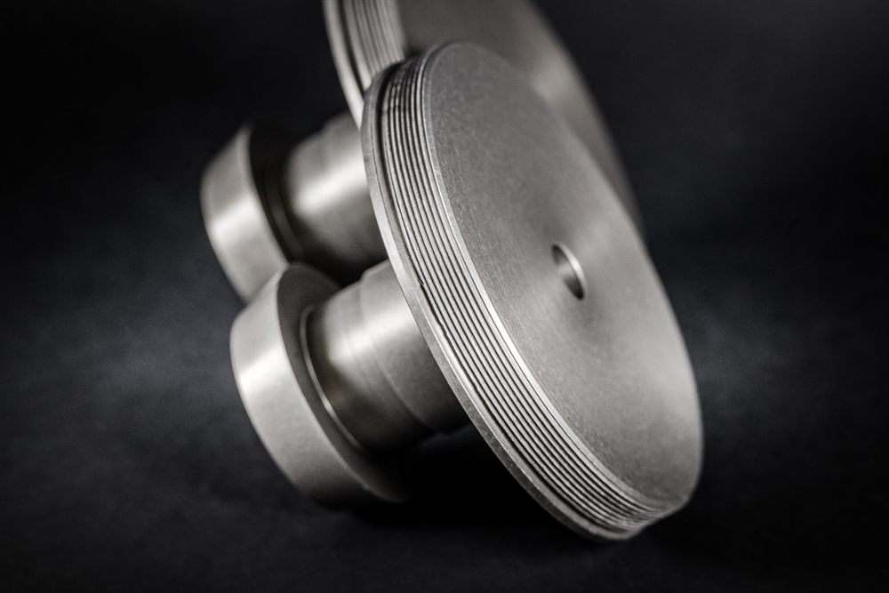 A precisely turned metal part with dense grooves along the edge and a central hole against a black background.