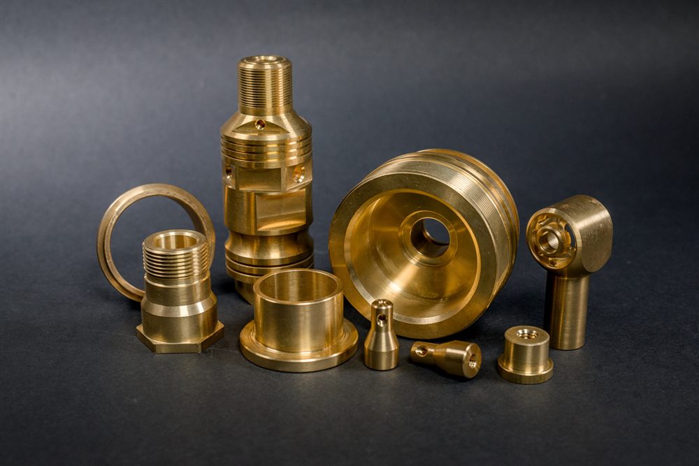 Brass components made using CNC machining technology, of various shapes and sizes, arranged against a dark background.