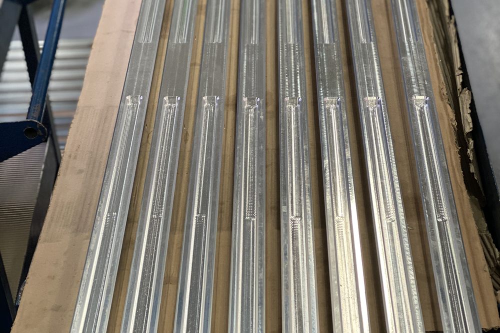 Long aluminium profiles with milled longitudinal grooves, laid side by side on brown cardboard.