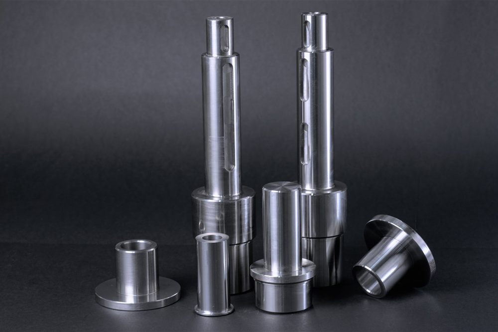 Machined metal shafts with milled keyways and lathe-turned sleeves with flanges, set against a dark background.