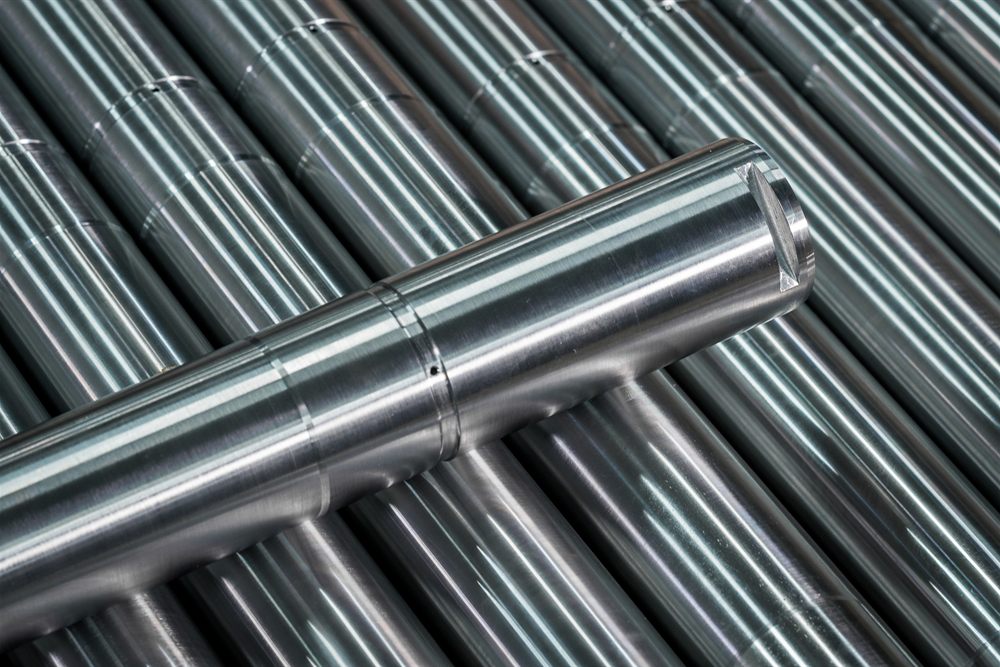 A steel shaft with a milled flat keyway lying on a stack of precisely machined cylindrical parts.