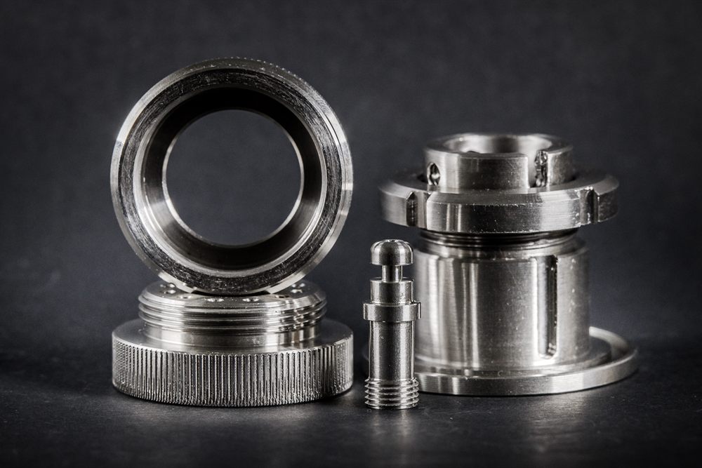 Precisely machined mechanical metal parts with threads, cut-outs and holes on a dark surface.