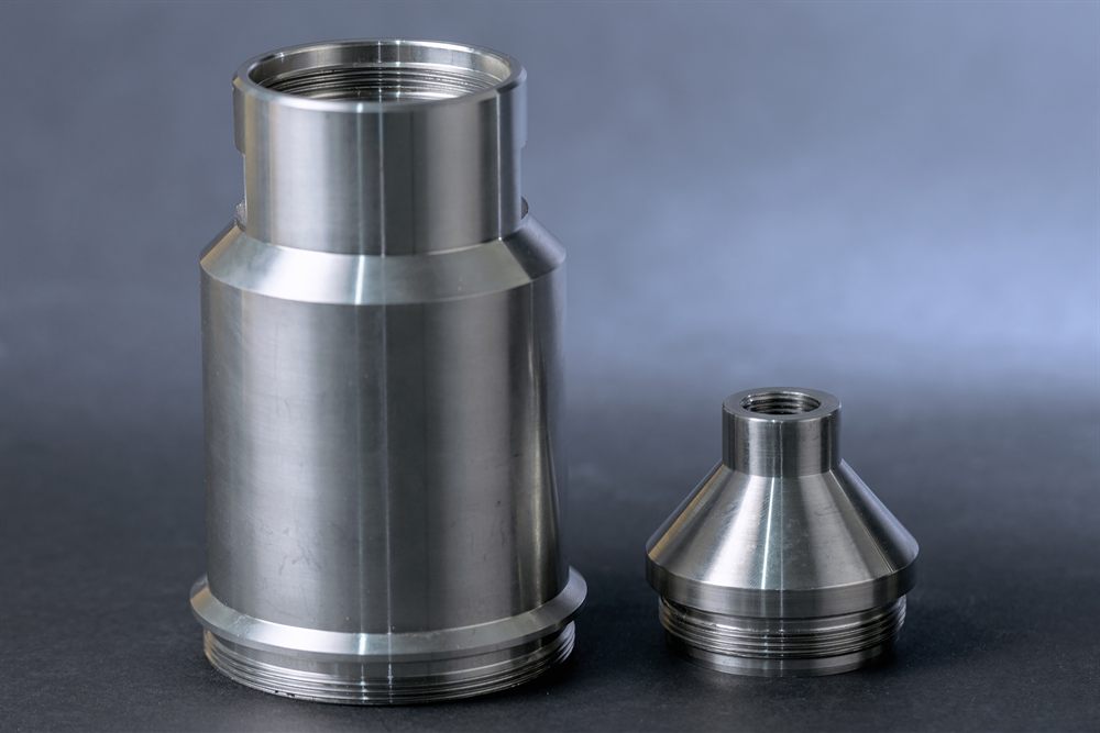 Two machined cylindrical metal parts with visible threads and a conical finish against a dark background.