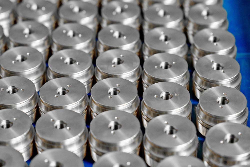Cylindrical metal parts with holes in the central section, lined up in rows on a blue surface.