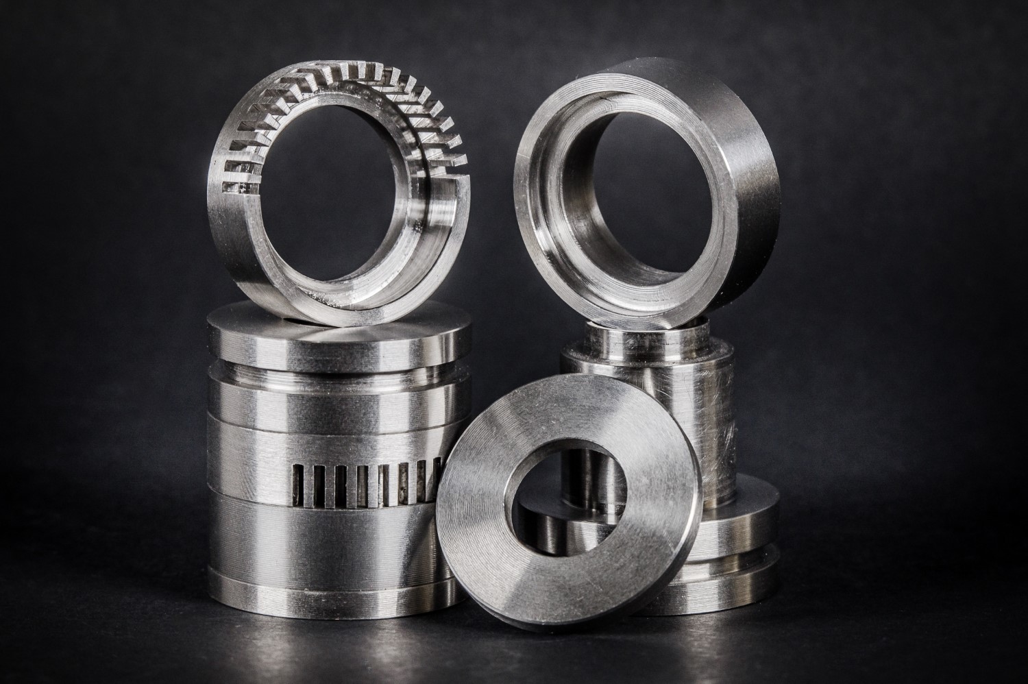Shiny silver metal components arranged in two tall stacks on a black background, with rings on top and alongside.