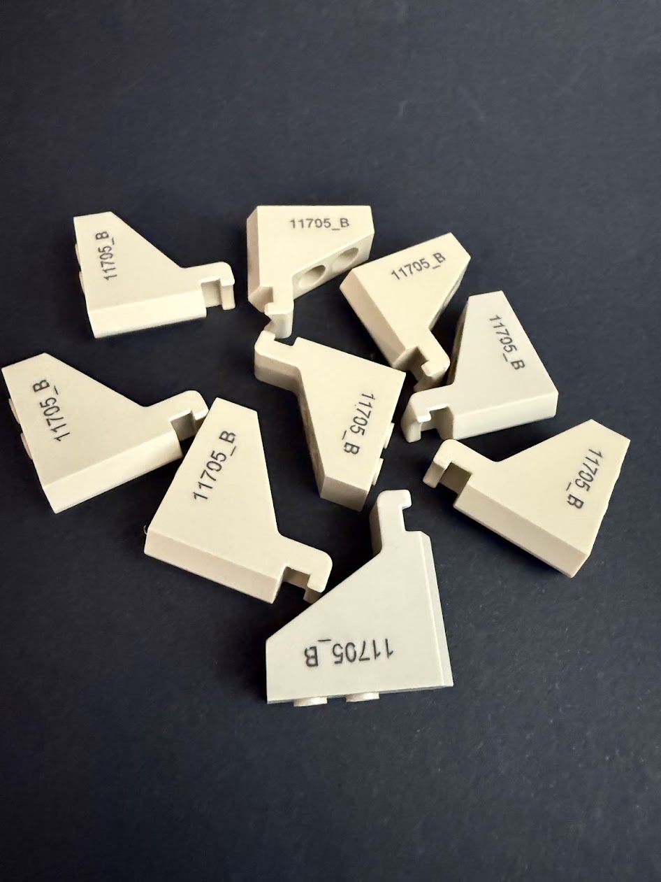 Beige plastic parts of trapezoidal shape with black markings arranged randomly on a dark surface.