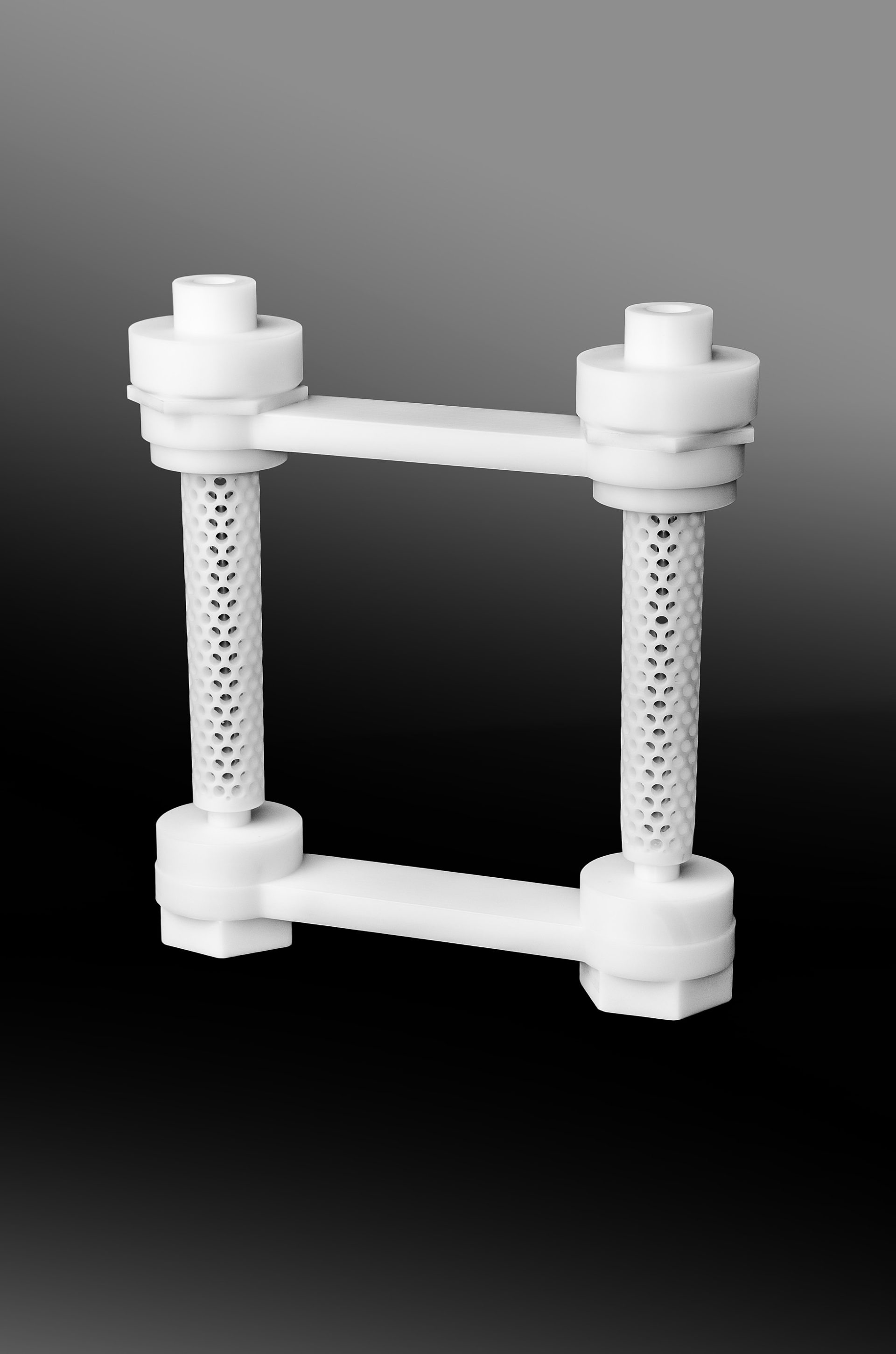 A white rectangular structure made of two vertical perforated cylinders joined at the bottom and top by horizontal beams.