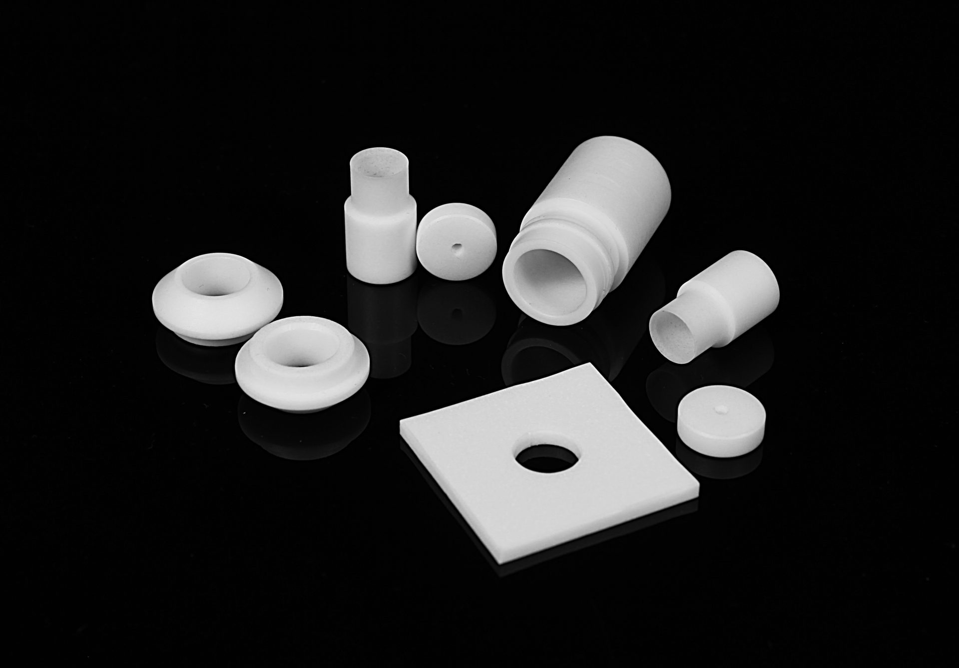 White smooth objects of various shapes against a black background, including a cylinder, a square plate and rings.