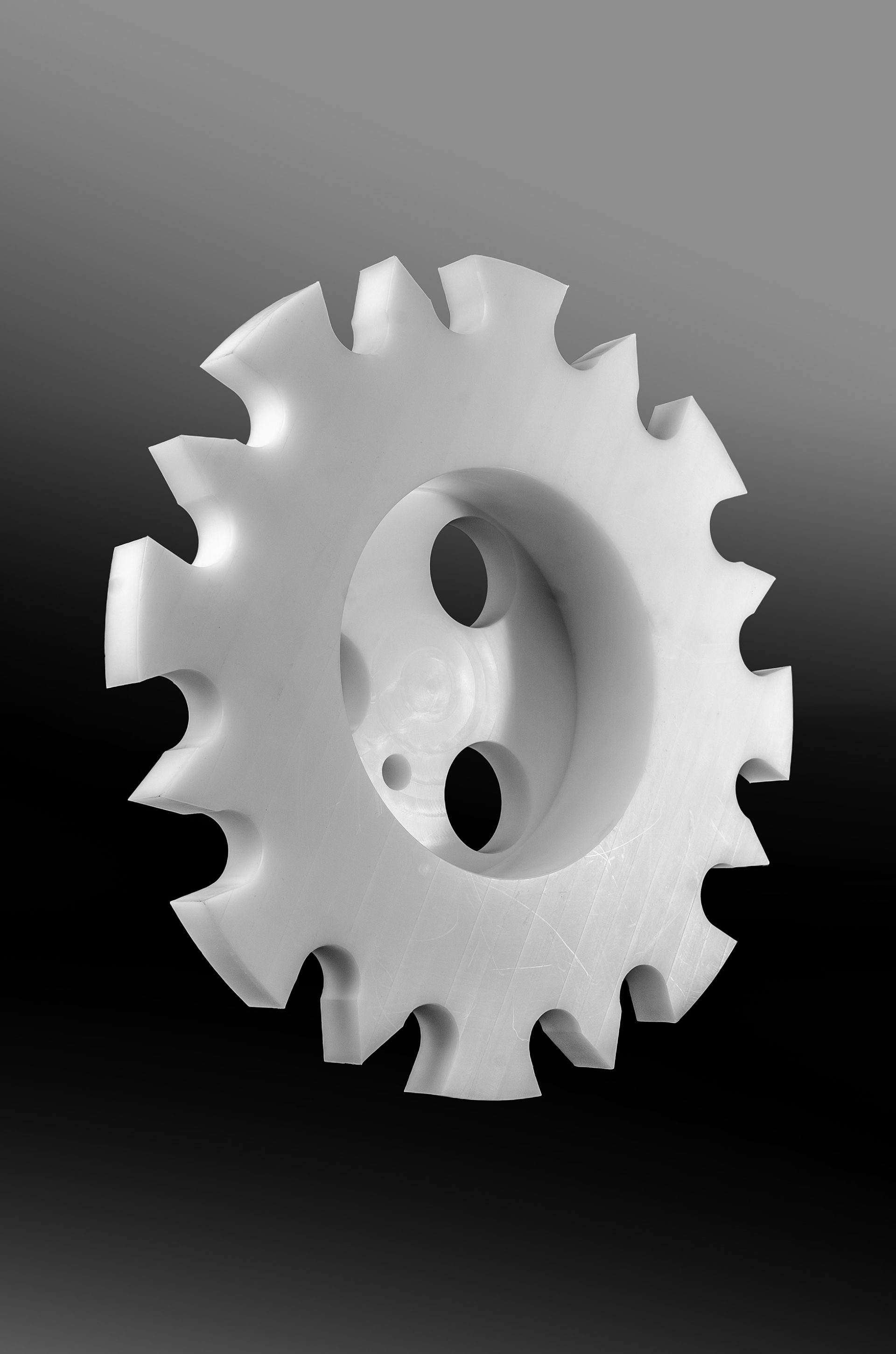 White plastic sprocket with three holes and evenly spaced teeth around the rim.
