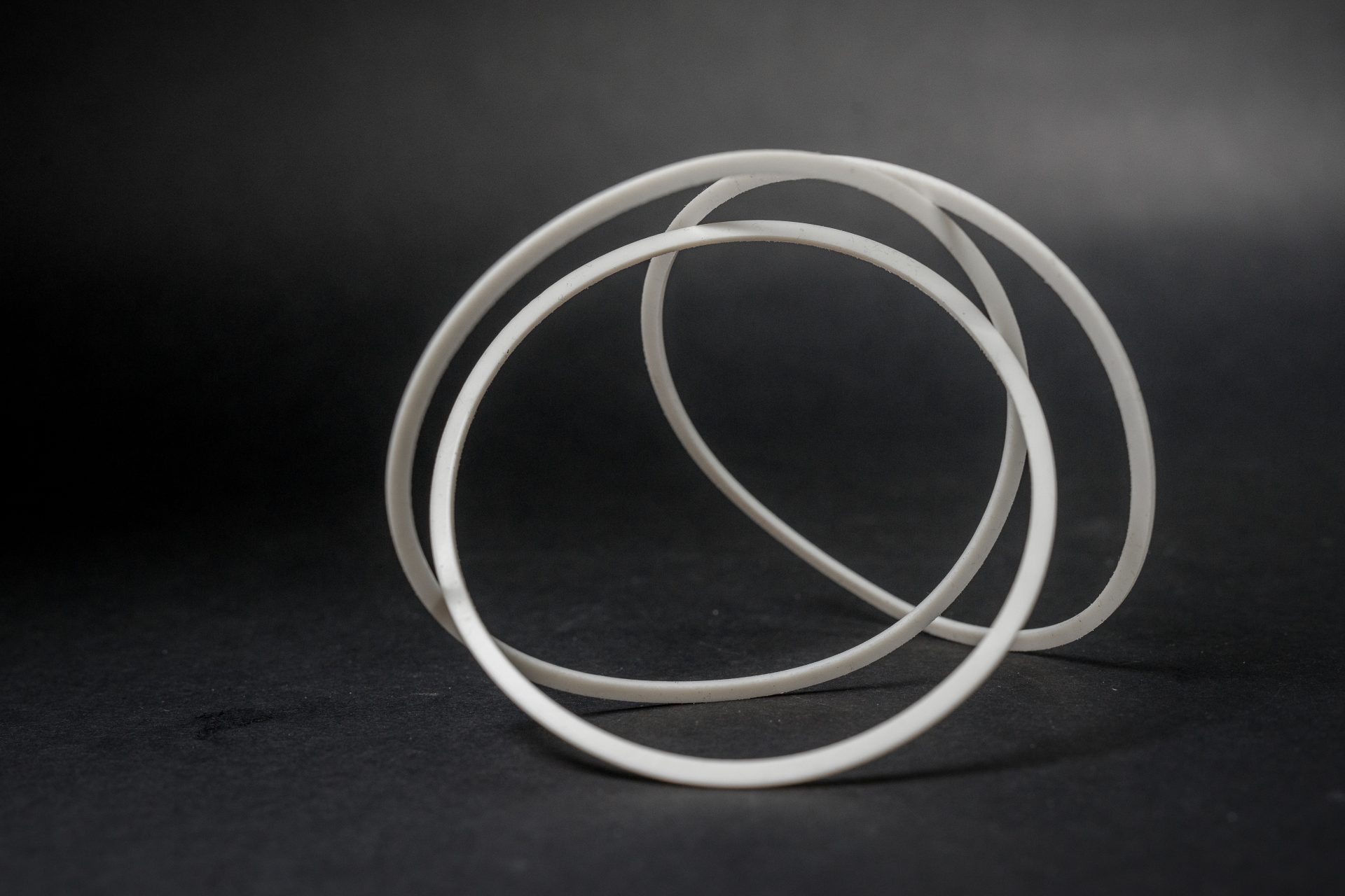 White matte rings with a flat profile form a three-dimensional composition arranged on a dark, smooth surface.