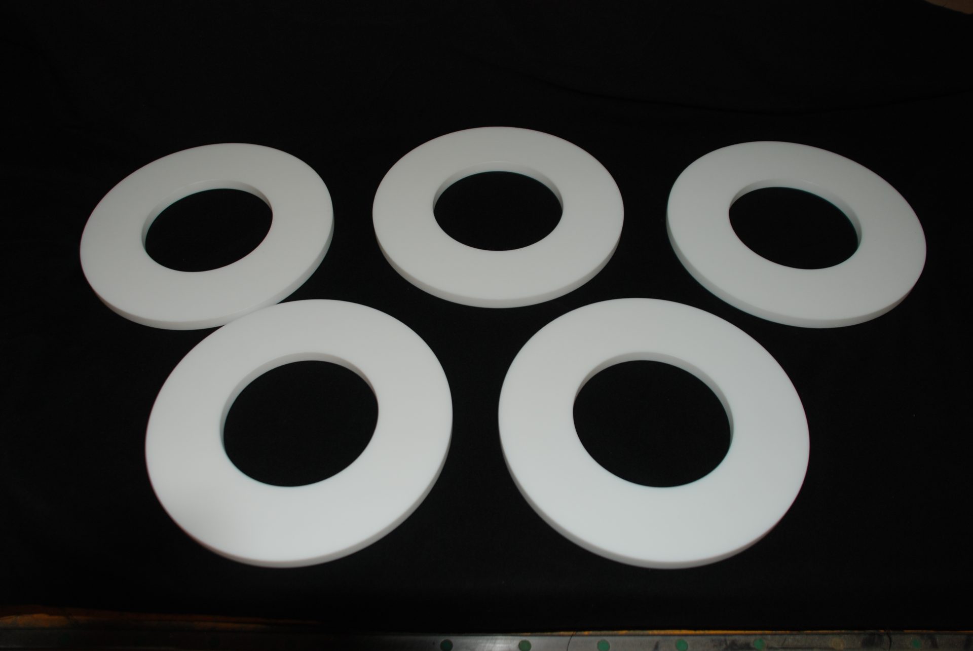 Five white sealing rings made of a smooth-surfaced polymer, arranged against a black background.