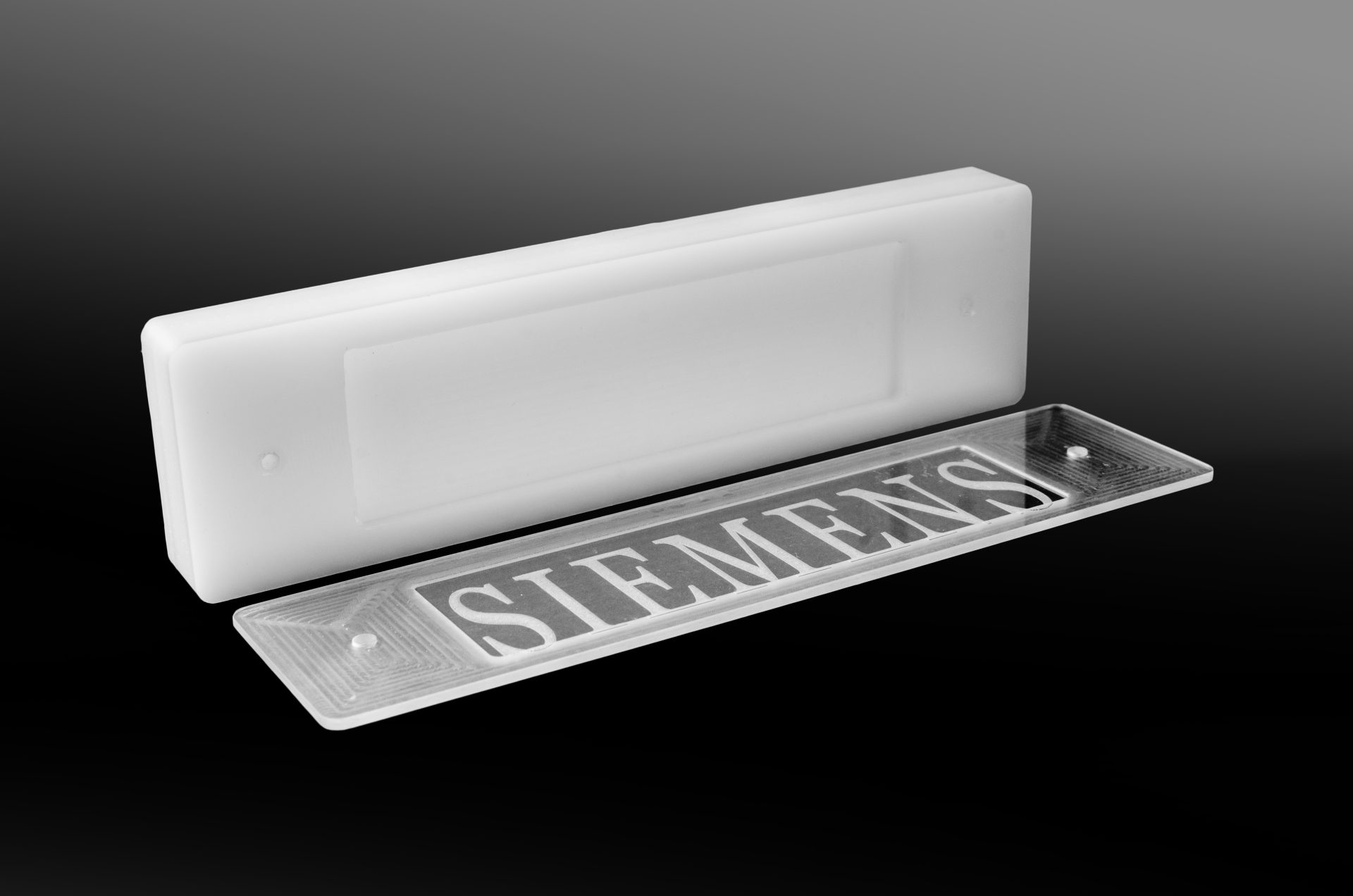 White plastic part and a transparent plate with the cut-out lettering SIEMENS set against a black background.