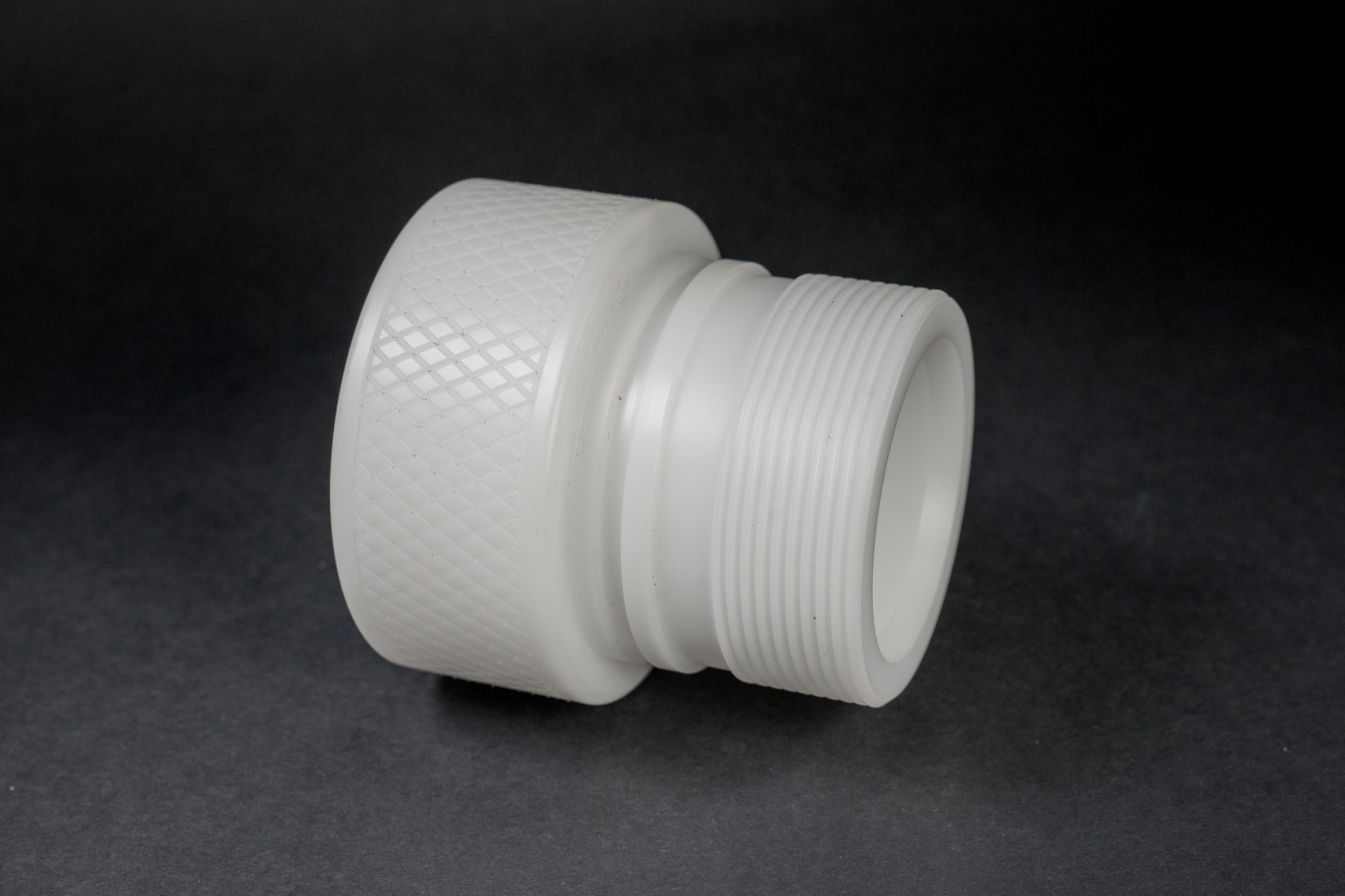 White plastic hydraulic adapter of cylindrical shape lying on a black, smooth and matte background.