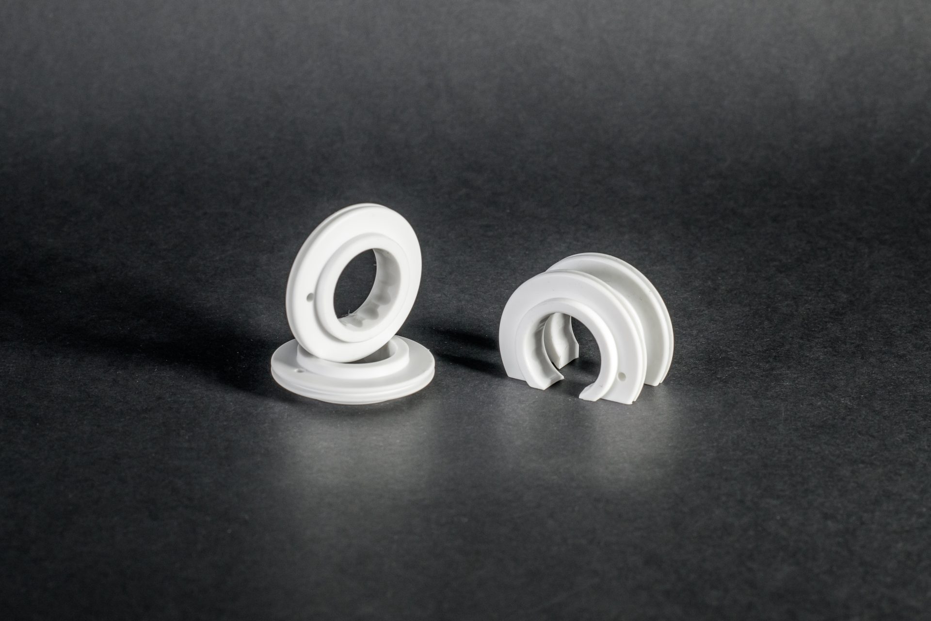 Four white ring- and half-ring-shaped parts with a profiled groove on a dark, matte background.