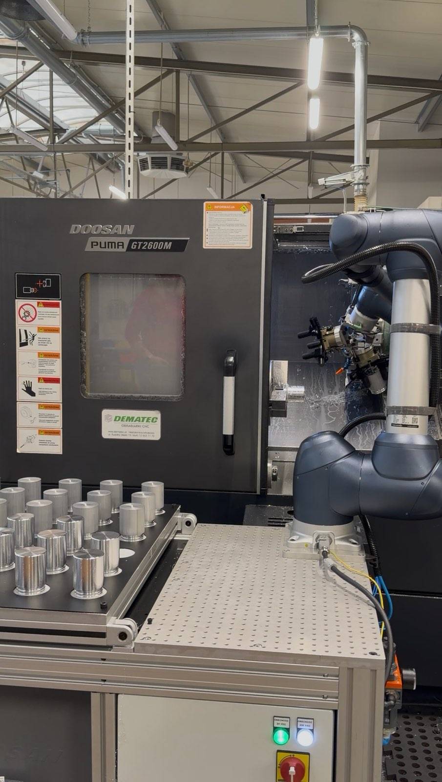 Doosan PUMA GT2600M CNC lathe and a robot arm next to a tray of cylindrical metal parts in the hall.