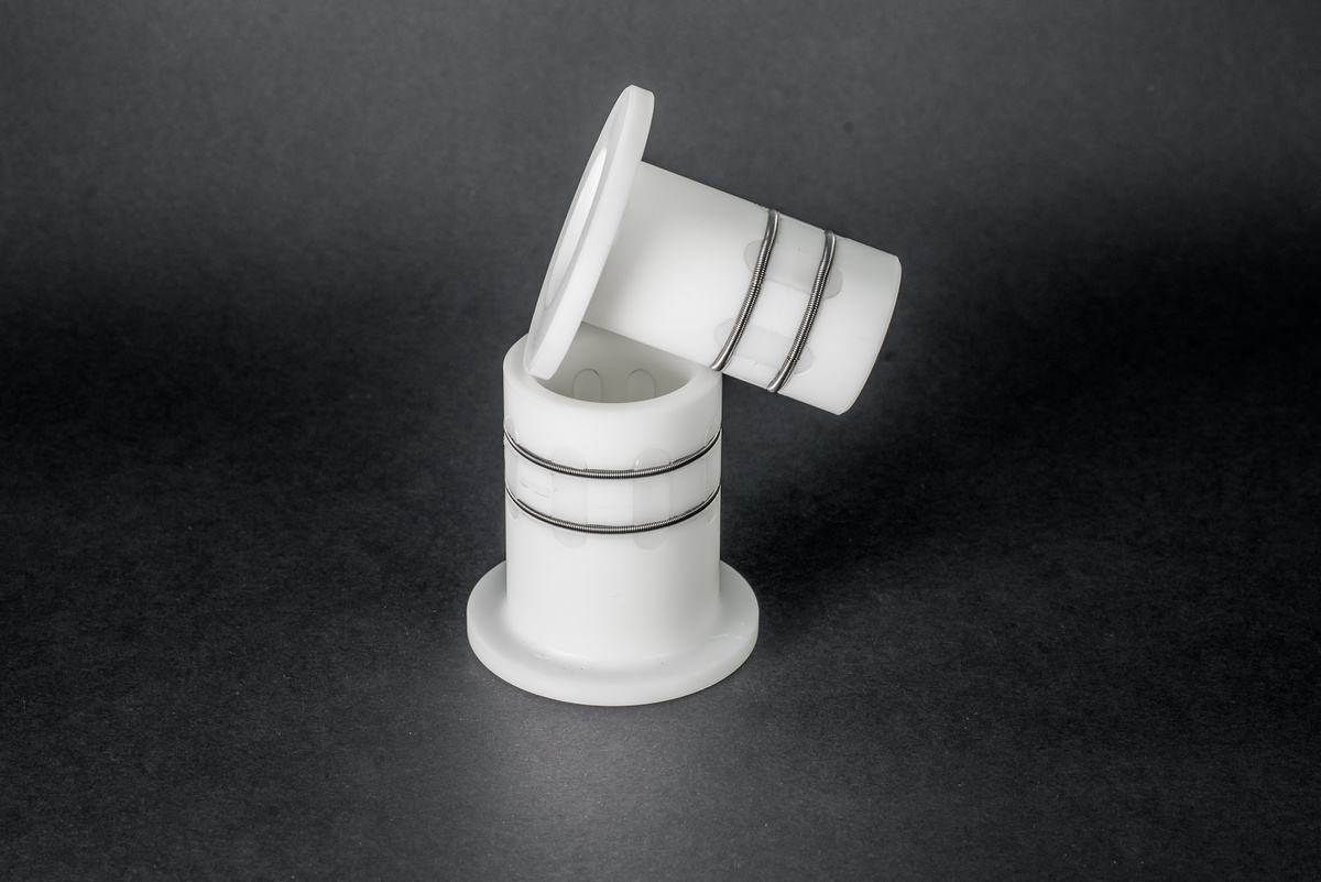 Two white plastic bushing components with a flange and two springs set against a smooth, dark background.