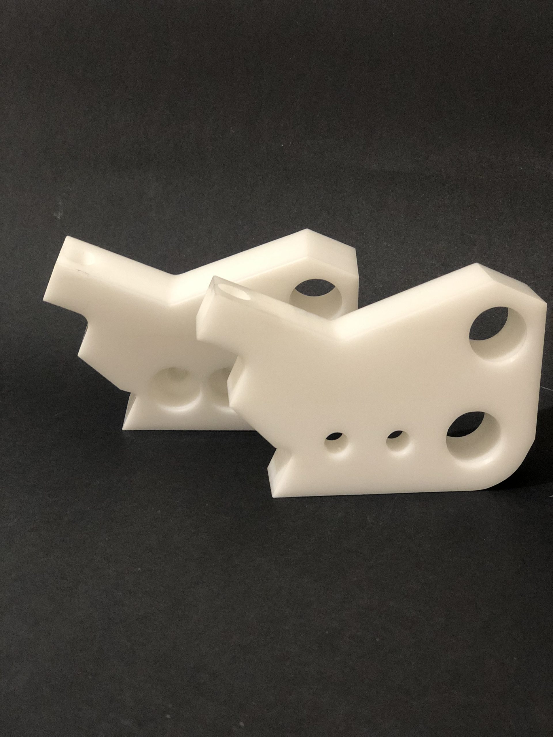 Two white plastic objects with irregular, angular shapes and holes lying against a black, matte background.