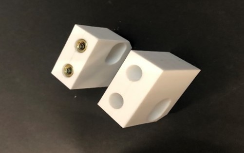 Two white chamfered plastic blocks with mounting holes and brass threads on a black background.
