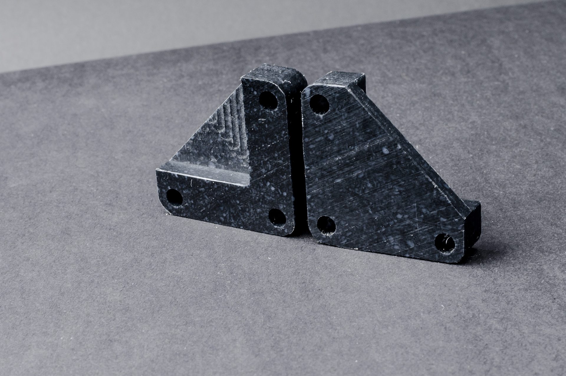 Two black profiled corner brackets with mounting holes touching each other on a grey work surface.