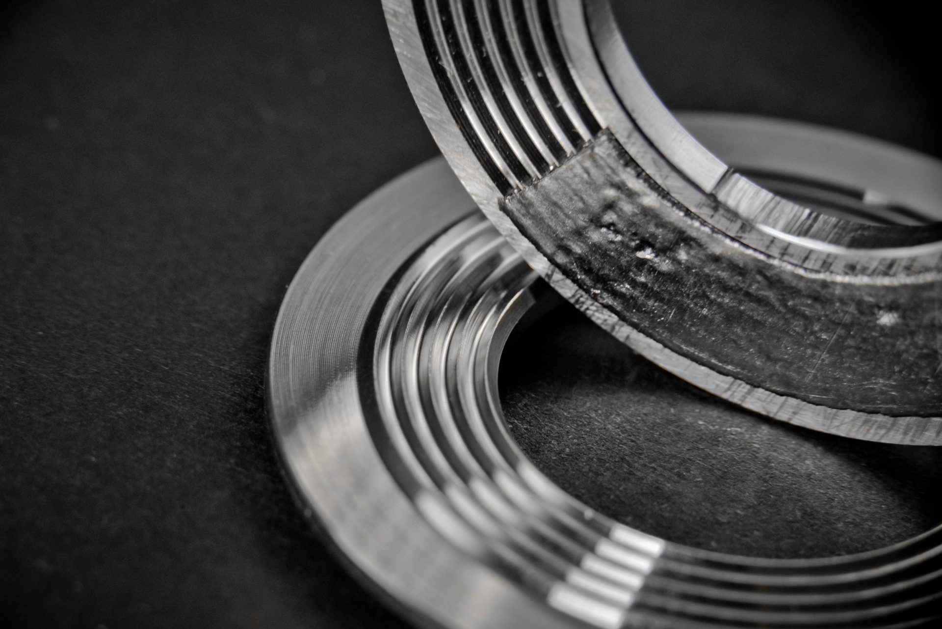 Two machined metal rings lying against a black background, one with a damaged surface.