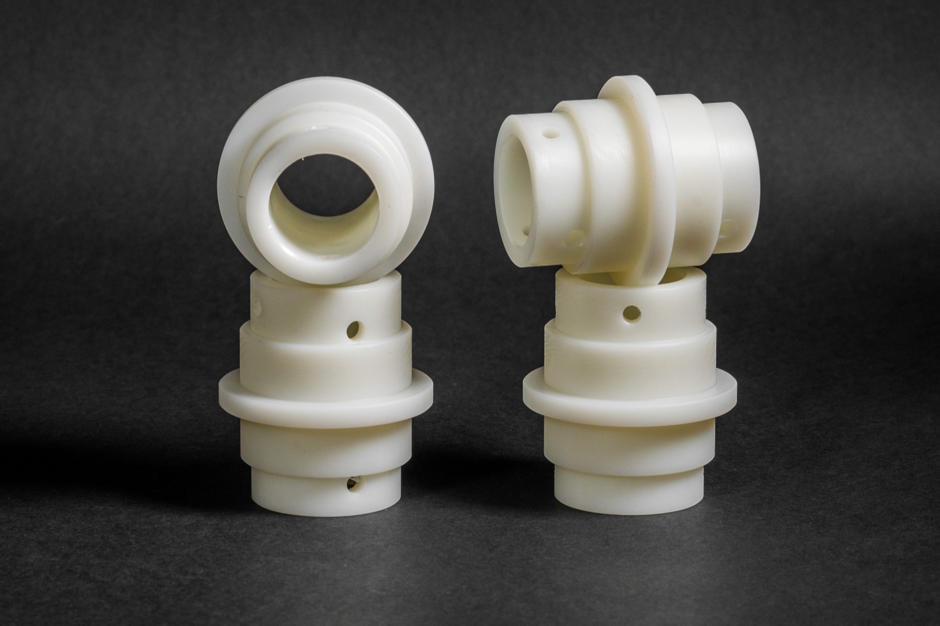Two upright and two lying white cylindrical components of varying diameter and with small holes against a background.