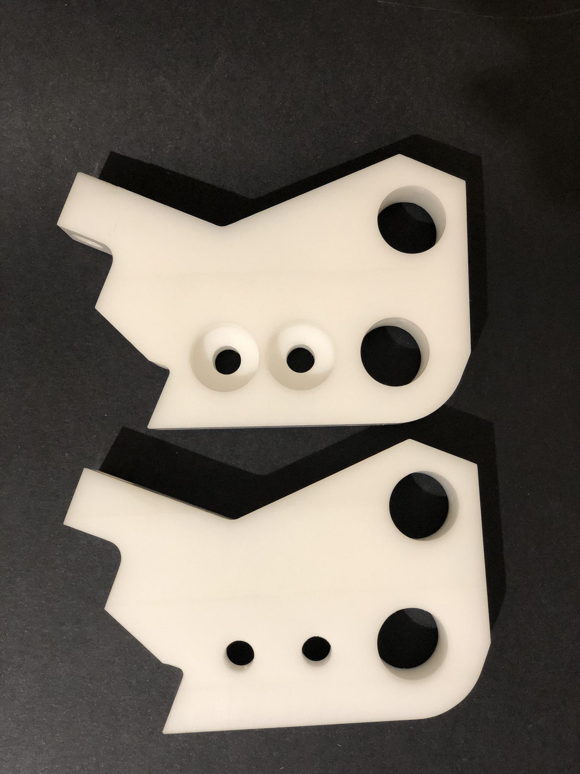 Two white profiled plastic plates with mounting holes and counterbores on a dark background.