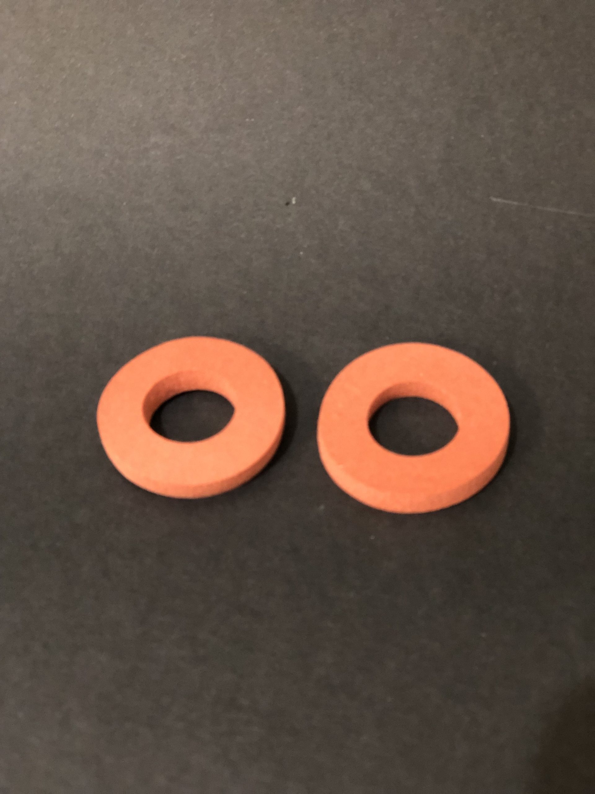 Two flat round orange washers with central holes, lying side by side on a dark background.