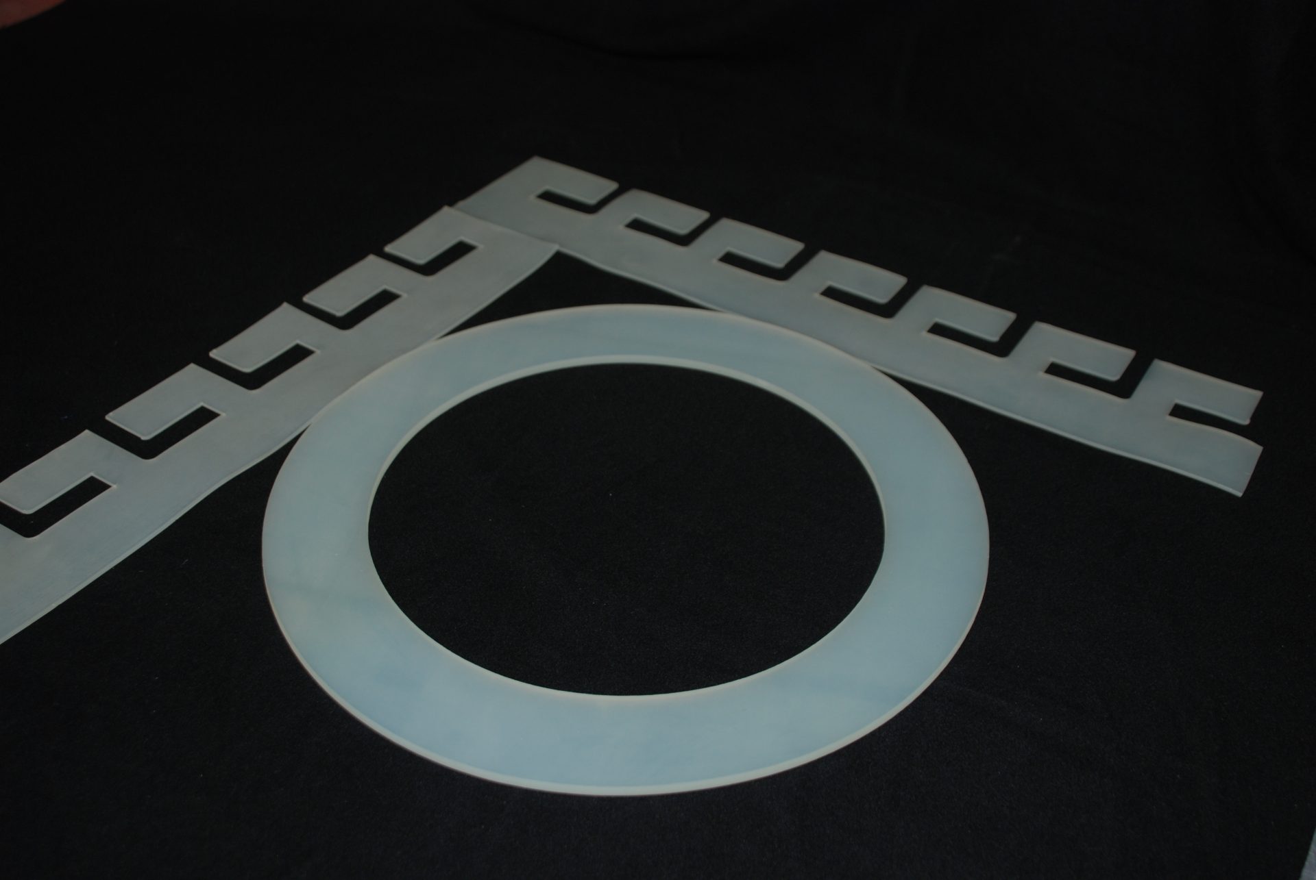 Light celadon flat ring lies on a black background next to two strips with a cut-out pattern arranged in a V shape.